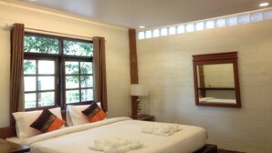 A hotel room with a large bed, a nightstand, a lamp, a window with curtains, and a mirror on the wall. - Treasure Inn Khaoyai (Pak Chong)
