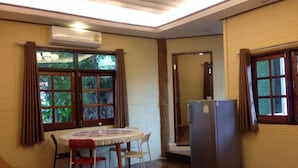 A room with a dining table, chairs, a refrigerator, and a window with curtains. - Treasure Inn Khaoyai (Pak Chong)