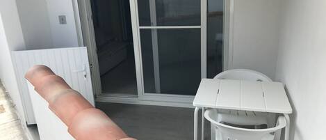 A room with a sliding glass door leading to a balcony, a white plastic chair, and a white table.