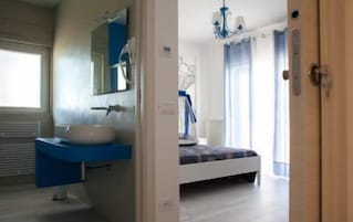 Une salle de bain moderne avec un lavabo blanc et un plan de toilette bleu, un grand miroir et une fenêtre avec des rideaux.