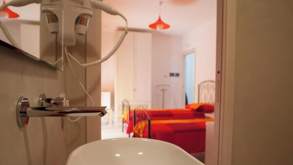 A bathroom with a sink and a mirror, a bed with a red blanket, and a red pendant light. - B&B Pentagramma (Alberobello)