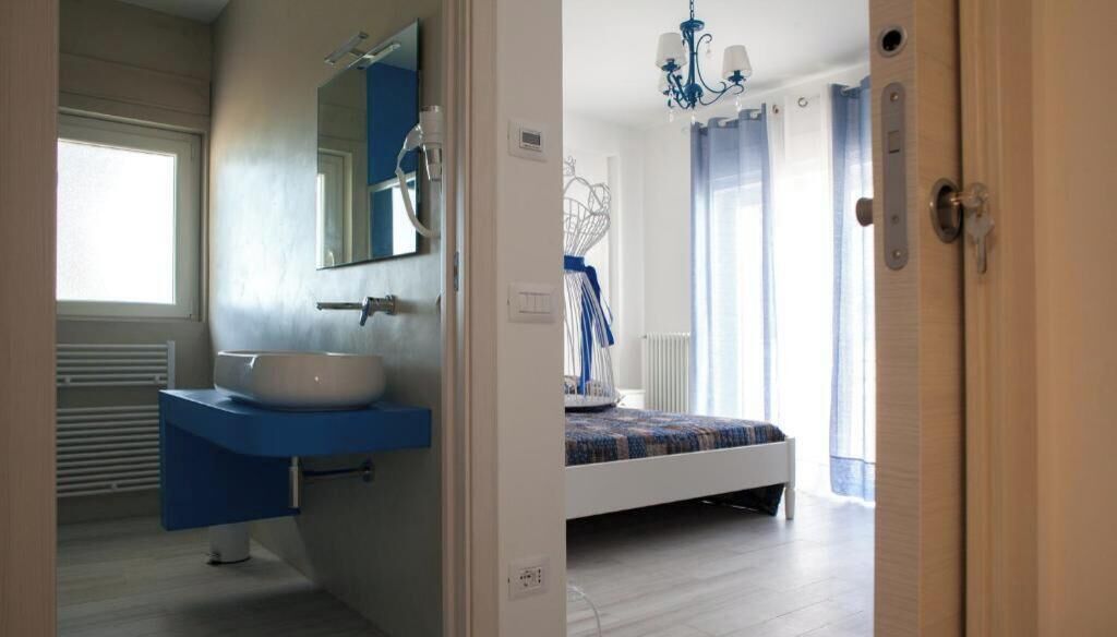 Un baño con lavamanos y espejo, una cama con colcha azul y blanca, y una araña.
