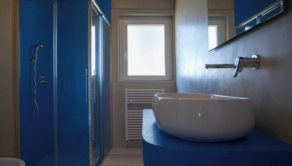 Une salle de bain dotée d’une douche à parois de verre, d’un lavabo blanc et d’une fenêtre laissant entrer la lumière naturelle.