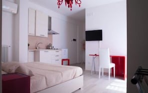 A bedroom with a bed, a desk, and a chair. There is a kitchenette with a stove and a sink. - B&B Pentagramma (Alberobello)