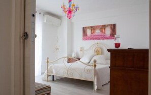 A bedroom with a white bed, a wooden dresser, and a painting on the wall. - B&B Pentagramma (Alberobello)