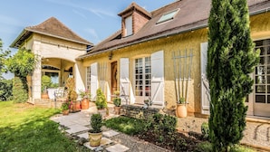 A two-story house with a stone facade, large windows, and a well-maintained garden with potted plants and a stone pathway. - Villa with Pool in Corrèze (Saint Bonnet La Rivière)