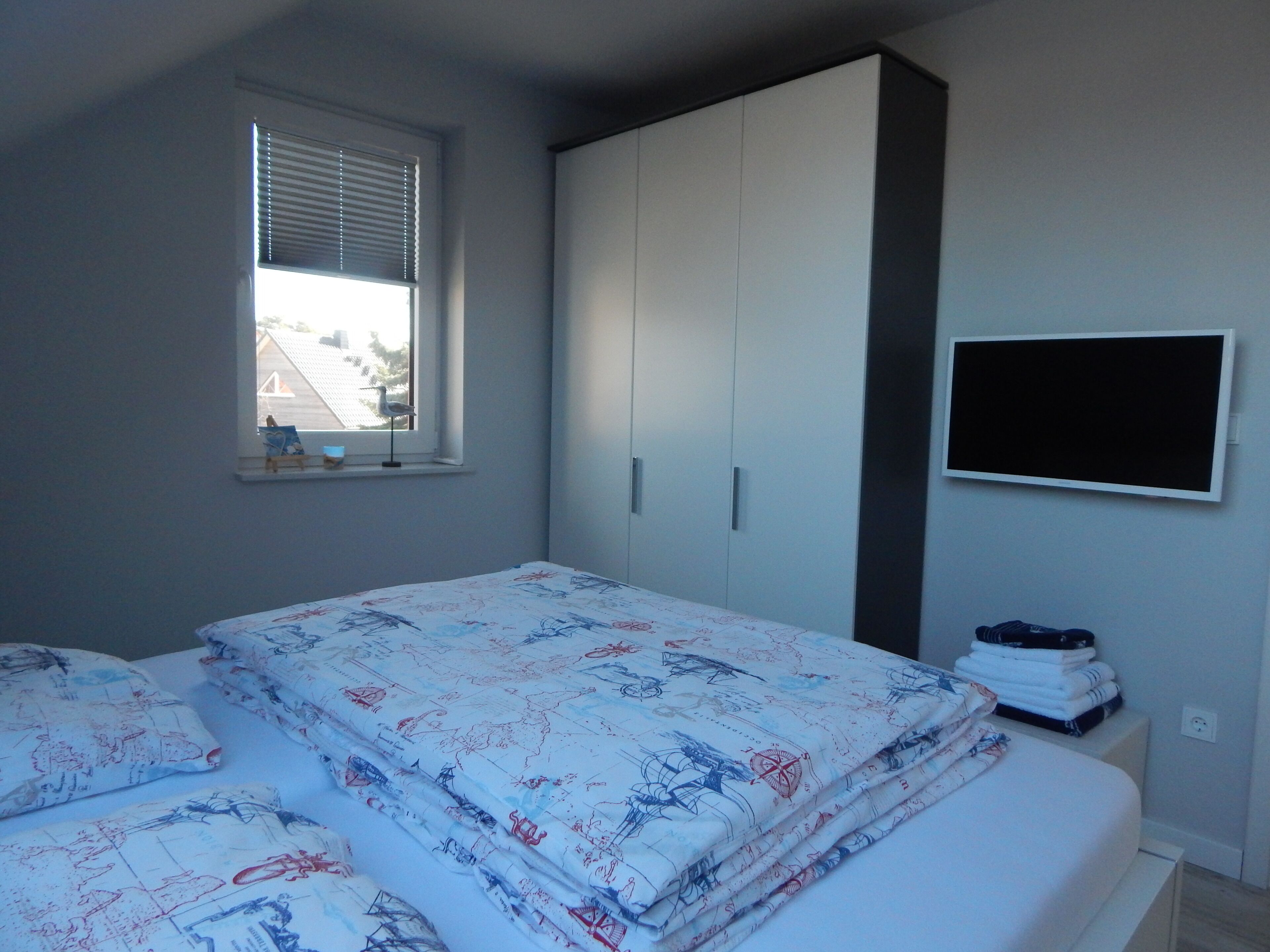 A bedroom with a bed, a wardrobe, a window, and a TV.