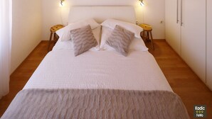 A bedroom with a wooden ceiling, a large bed with white bedding, two bedside tables, and a wardrobe.
