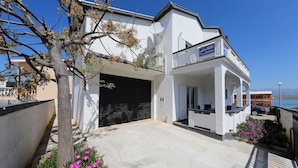 A modern two-story building with a garage, a covered outdoor seating area, and a view of the sea.