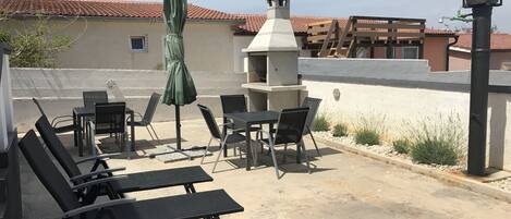 An outdoor patio with lounge chairs, a table, and a grill.