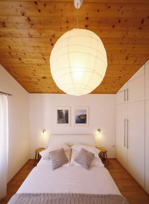 Une chambre avec un plafond en bois, un grand lit avec une literie blanche, deux tables de chevet et une armoire.