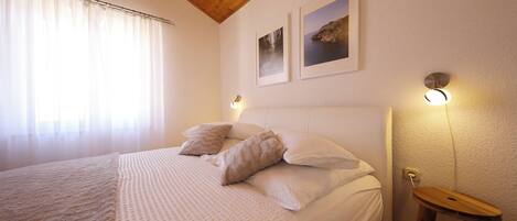A bedroom with a large bed, wooden ceiling, two wall-mounted lights, and a small wooden stool.