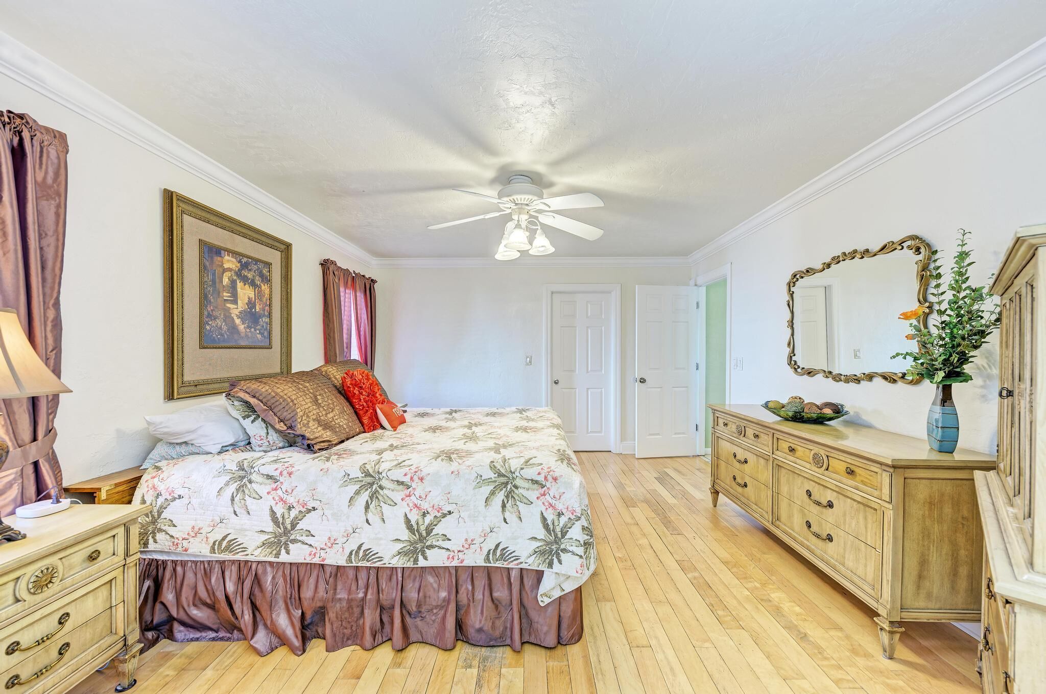 Une chambre à coucher avec un lit, une commode, un ventilateur de plafond et un miroir.