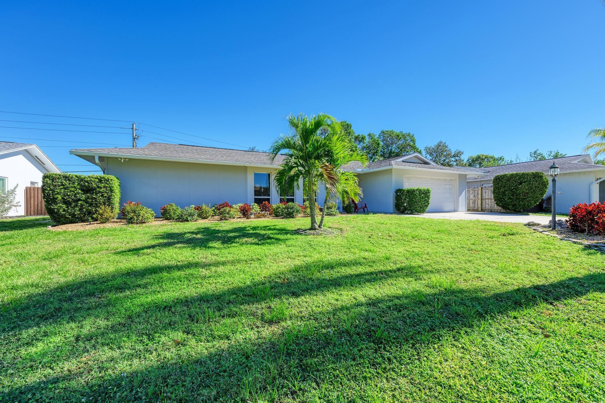 A residential house with a well-maintained lawn, a palm tree, and various shrubs.