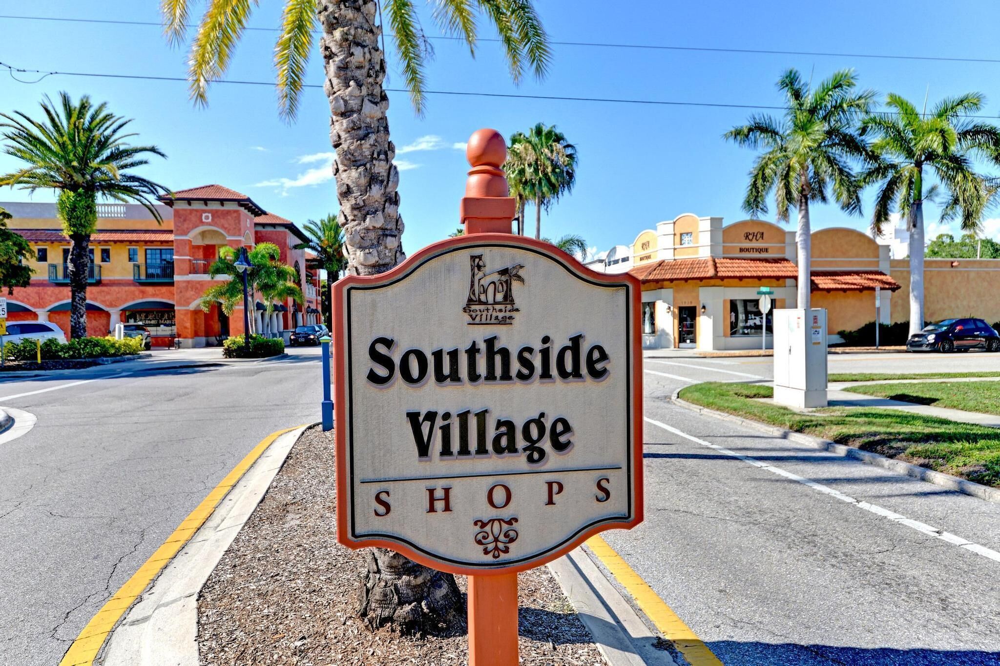 A sign for Southside Village Shops with a clear view of the surrounding area including palm trees and buildings.