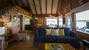 A cozy cabin interior with a blue sofa, a wooden dining table, and a view of a lake. - Door County's Chalet On The Shore (Sturgeon Bay)
