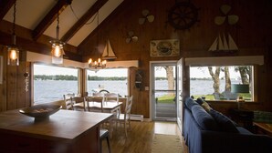 A wooden interior with a dining area, a sofa, and a view of the lake. - Door County's Chalet On The Shore (Sturgeon Bay)