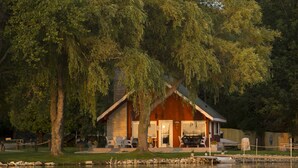 A lakeside cabin with a deck, outdoor seating, and a view of the water. - Door County's Chalet On The Shore (Sturgeon Bay)