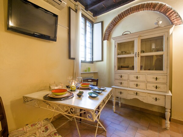 A dining area with a table set for four, a white cabinet with glass doors, and a flat-screen TV mounted on the wall.