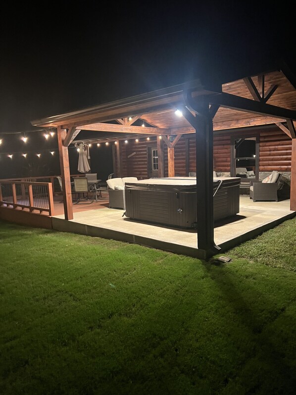 Un patio exterior con una zona de estar cubierta, un jacuzzi y luces colgantes.