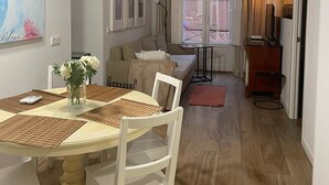 A dining area with a round table, white chairs, and a vase of flowers. There is a sofa and a TV stand in the background. - Exterior, balconies, terrace, 2 bathrooms, wifi, next to subway and train. (Madrid)