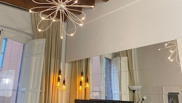 A modern interior with exposed wooden beams, a large mirror, a flat-screen TV, and a unique star-shaped pendant light. - Exterior, balconies, terrace, 2 bathrooms, wifi, next to subway and train. (Madrid)