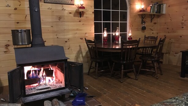 Una habitación acogedora con estufa de leña, paredes de madera, una mesa de comedor con sillas y una ventana con vistas.