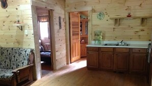 Un interior de madera con un sofá, una zona de cocina y un acceso a otra habitación.