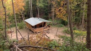 Una cabaña en un bosque con terraza de madera y techo de metal.