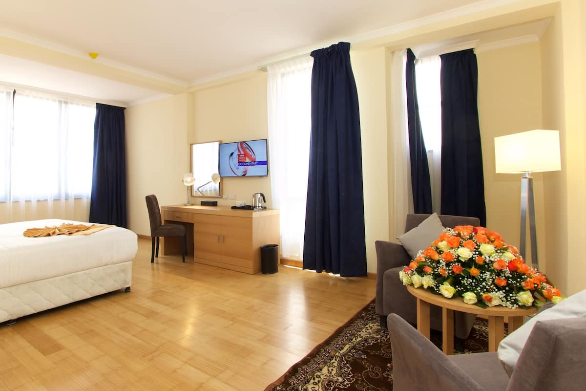 A hotel room with a bed, desk, chair, and a small table with flowers.