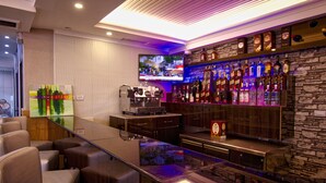 Een bar met een flatscreen televisie, een koffieapparaat en verschillende flessen drank.
