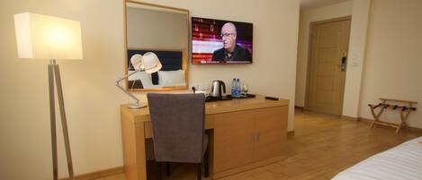 Una habitación de hotel con escritorio, silla, lámpara, televisión y cama.