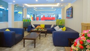 Een moderne lobby met een blauwe zithoek, een houten salontafel en een bloemstuk.