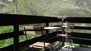 Eine Holzdar Terrasse mit Bänken und Tischen mit Blick auf eine gebirgige Landschaft, die mit Schneeflecken durchzogen ist.