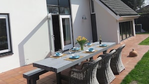 Une maison moderne avec une table de patio mise en place pour les repas, entourée de chaises en osier.