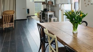 Un coin repas avec une table et des chaises en bois, un vase de fleurs et une suspension.