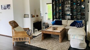 Un salon avec une cheminée, une bibliothèque et une table basse en osier.