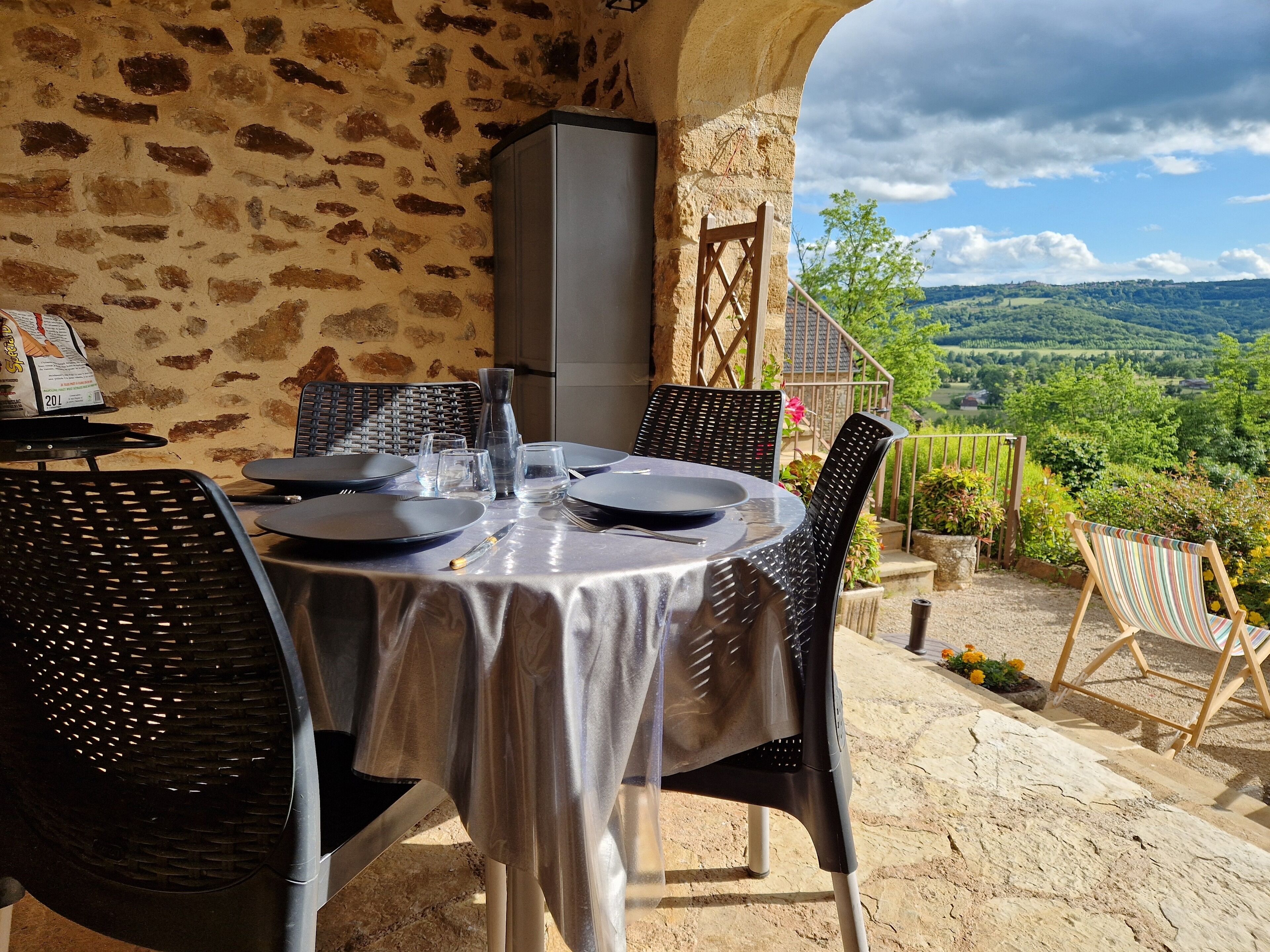Mesa para dos con un fondo de pared de piedra, vistas a colinas verdes y una silla de madera con cojín a rayas.
