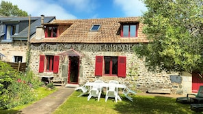 A stone house with red shutters, a small garden, and a patio with outdoor furniture.