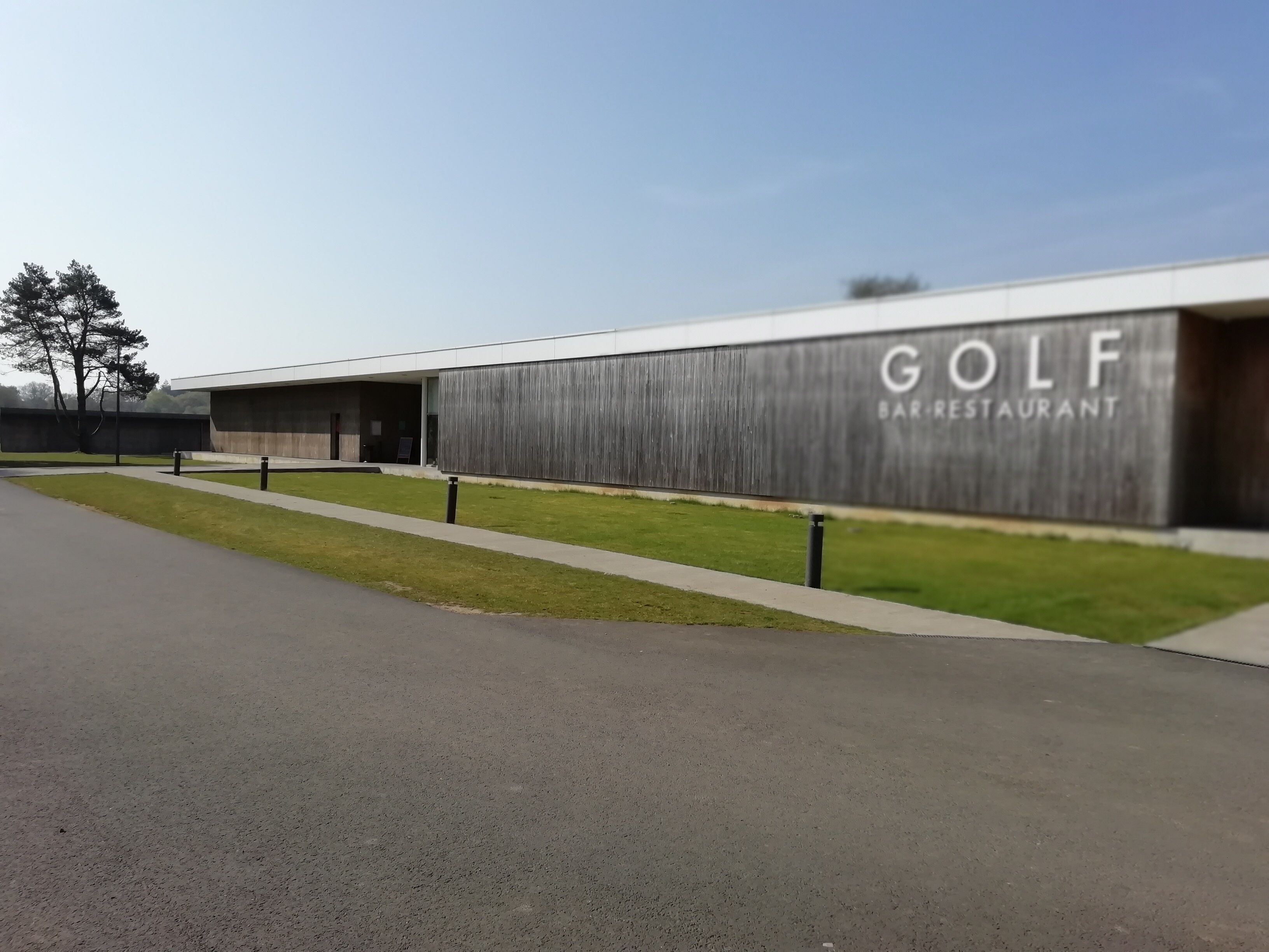 Un bâtiment moderne avec une enseigne indiquant : « BAR-RESTAURANT DE GOLF ».
