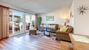 A living room with a sofa, armchairs, a coffee table, and a dining table. There is a large window with curtains, a plant, and a colorful wall clock. - La Jolla Shores 'Ocean Breeze Getaway', large patio, partial ocean view,sunsets (San Diego)