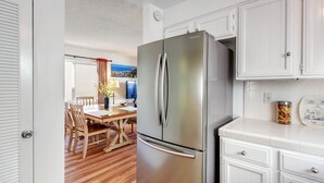 A modern kitchen with a stainless steel refrigerator, wooden dining table, and white cabinetry. - La Jolla Shores 'Ocean Breeze Getaway', large patio, partial ocean view,sunsets (San Diego)