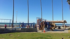 A beach playground with slides and climbing structures, palm trees, and a clear blue sky. - La Jolla Shores 'Ocean Breeze Getaway', large patio, partial ocean view,sunsets (San Diego)
