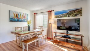 A dining area with a wooden table and chairs, a TV on a wooden stand, and artwork on the walls. - La Jolla Shores 'Ocean Breeze Getaway', large patio, partial ocean view,sunsets (San Diego)