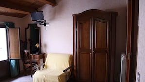 Una habitación con un armario de madera, una silla tapizada, un escritorio y un televisor fijado a la pared.