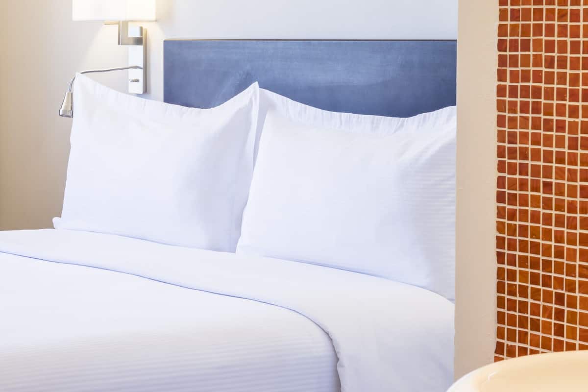 Une chambre d’hôtel avec un lit bien fait, une lampe de chevet et un mur recouvert de carreaux.