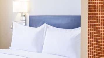 Ein Hotelzimmer mit einem ordentlich bezogenen Bett, einer Nachttischlampe und einer gefliesten Wand.