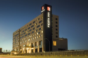 Un hotel de varios pisos con un llamativo letrero de 'Fiesta Inn' en la fachada, que presenta un diseño arquitectónico moderno con ventanas uniformemente distribuidas y un techo plano.