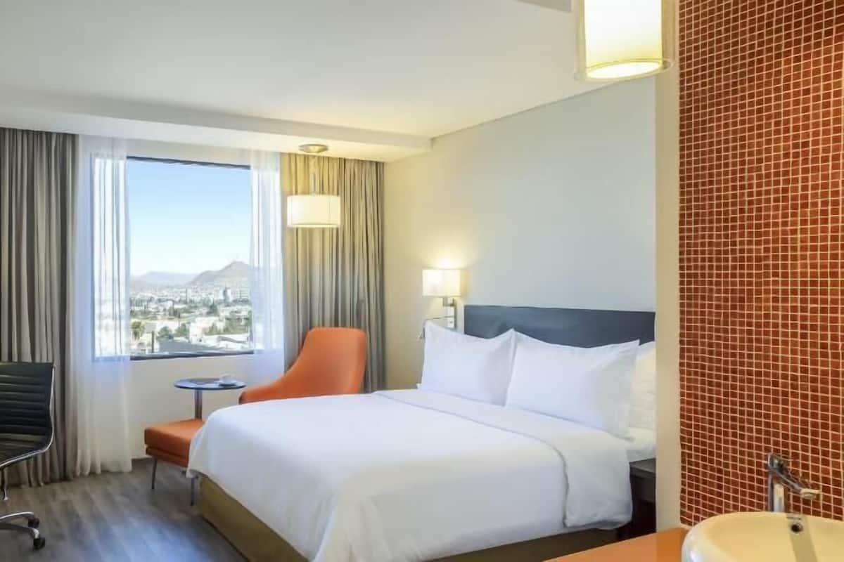Une chambre d’hôtel équipée d’un lit, d’un bureau, d’une chaise, d’une télévision et offrant une vue sur le paysage urbain.