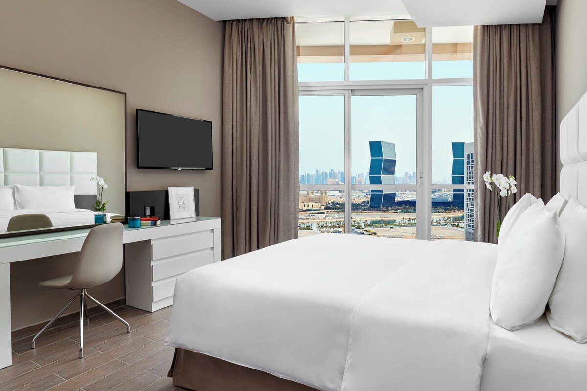 A modern hotel room with a large bed, a desk, and a TV.